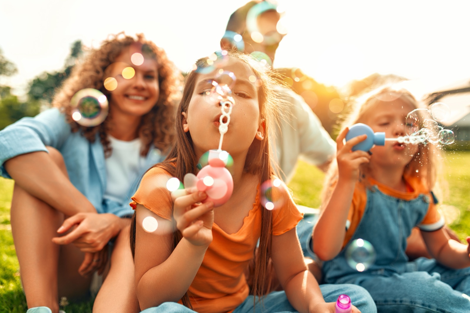 Two children blow bubbles outdoors with their family on a sunny day